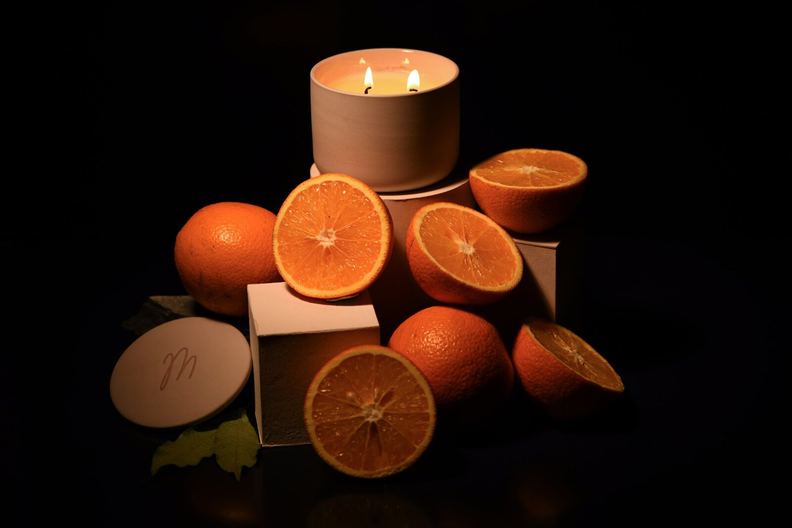 Candle with halved oranges lit low against black
